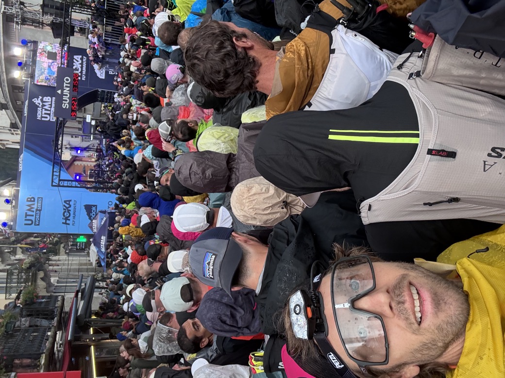 Packed start pen under the UTMB arch in Chamonix, runners in rain jackets