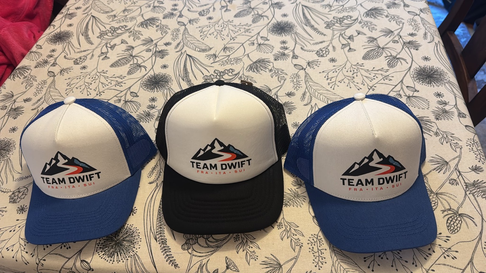 Three Team DWIFT trucker hats laid out on a table